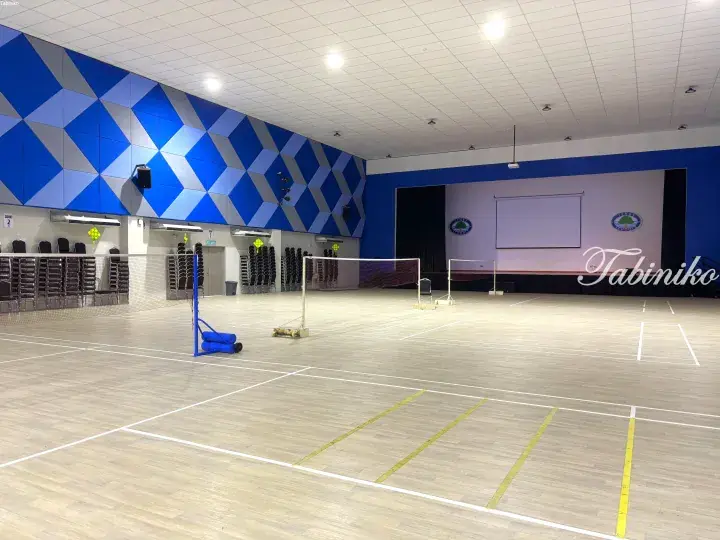 Spacious indoor badminton court with blue geometric wall panels and a stage at Tenby Schools.