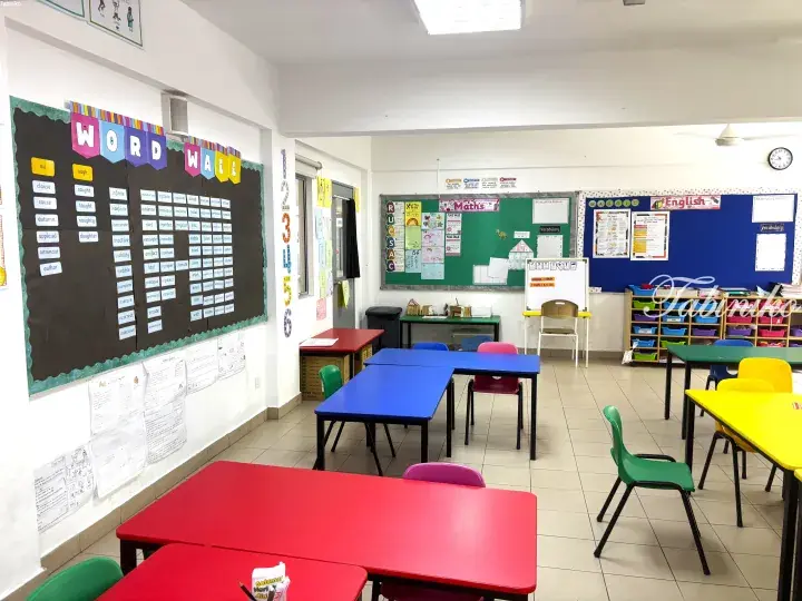 Bright classroom with colorful tables, chairs, and educational word wall displays.