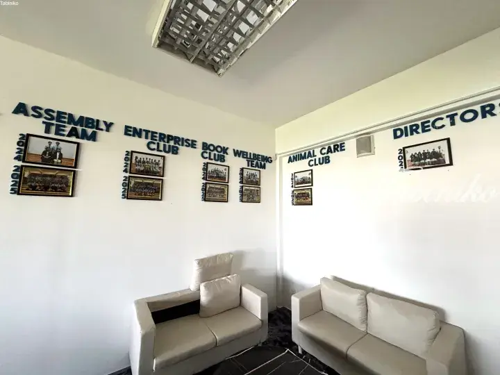 White lounge area with framed photos of student clubs like Assembly Team and Directors on the wall.