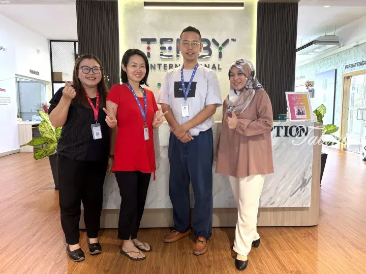 Four smiling staff members posing in front of the Tenby International School reception desk.