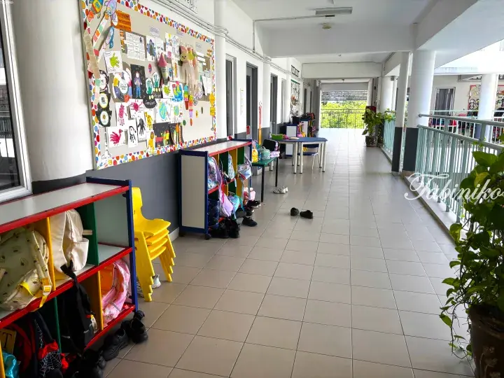Bright school corridor with colorful student artwork on display boards, low shelves holding backpacks, and yellow chairs.