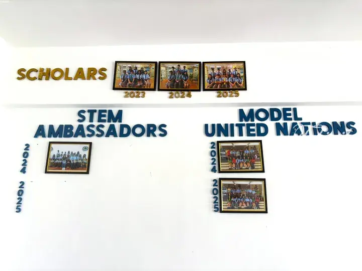 Wall display featuring framed photos of student groups under SCHOLARS, STEM AMBASSADORS, and MODEL UNITED NATIONS headings with years 2023-2025.