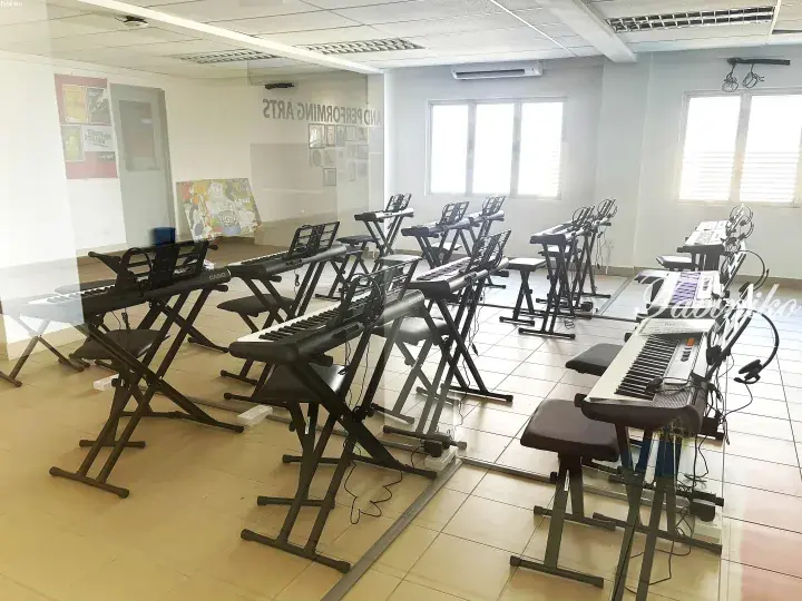 Rows of Casio keyboards on stands in a bright music classroom with mirrors and windows.
