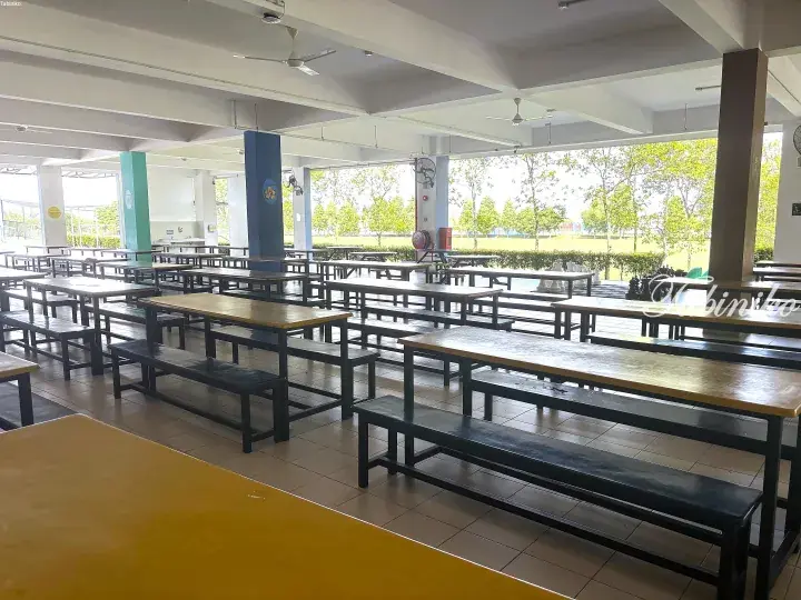 Spacious open-air school canteen with long wooden tables and benches overlooking a green field.