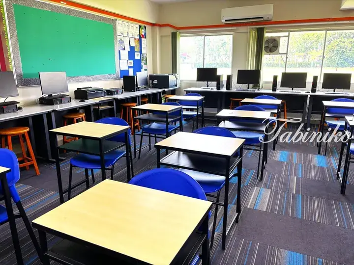 Modern classroom with blue chairs, wooden desks, and computer stations near large windows.