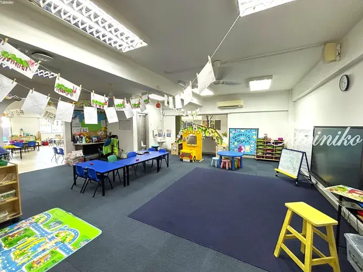 Bright classroom with children’s artwork, blue tables, and a play bus in a Malaysia preschool.