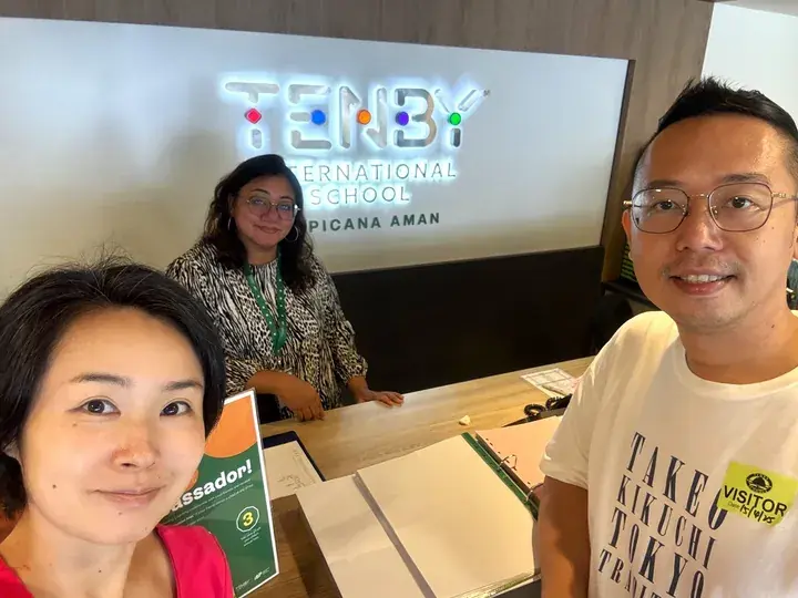 A family visits Tenby International School at Picana Aman, standing at the reception desk with the school logo visible.