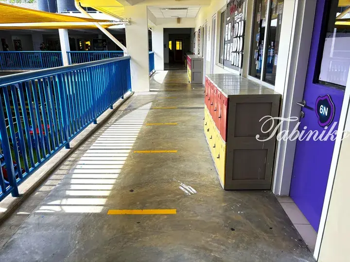 Sunlit school corridor with blue railings, yellow floor markers, and colorful lockers outside a purple classroom door.
