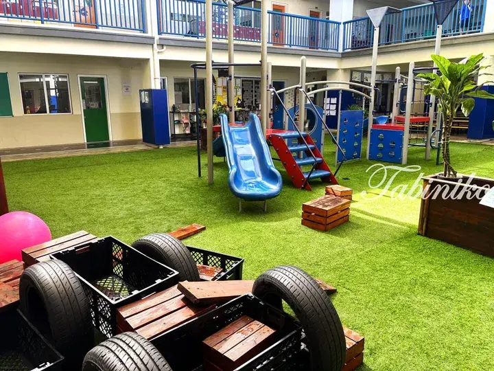 Colorful playground with slides and climbing frames on green artificial turf at an indoor school facility.
