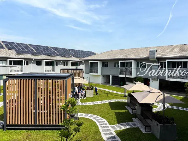 Modern two-story residential building with solar panels, landscaped courtyard, and shaded seating area.