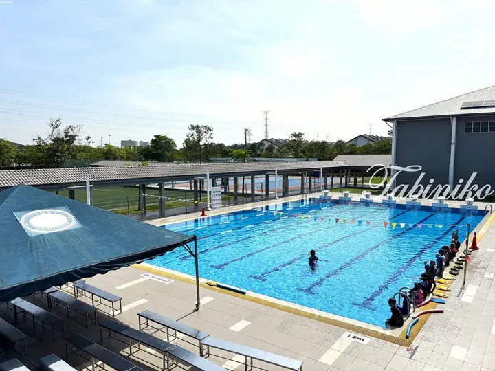 Outdoor swimming pool at Tenby Schools with students practicing, surrounded by covered walkways and seating areas.