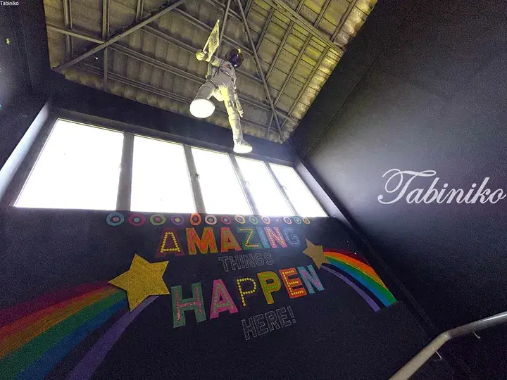Astronaut figure hanging from ceiling above colorful ‘Amazing Things Happen Here’ wall mural with rainbow and stars.
