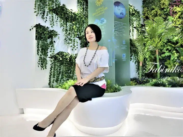 Woman sitting on a white curved bench in front of a green living wall display about Kuala Lumpur’s climate.