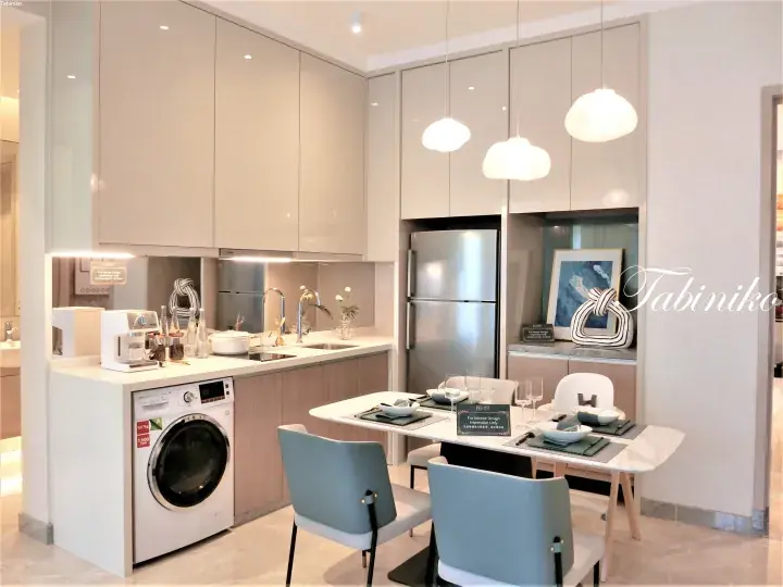 Modern kitchen with light cabinetry, stainless steel fridge, washing machine, and dining table with blue chairs.