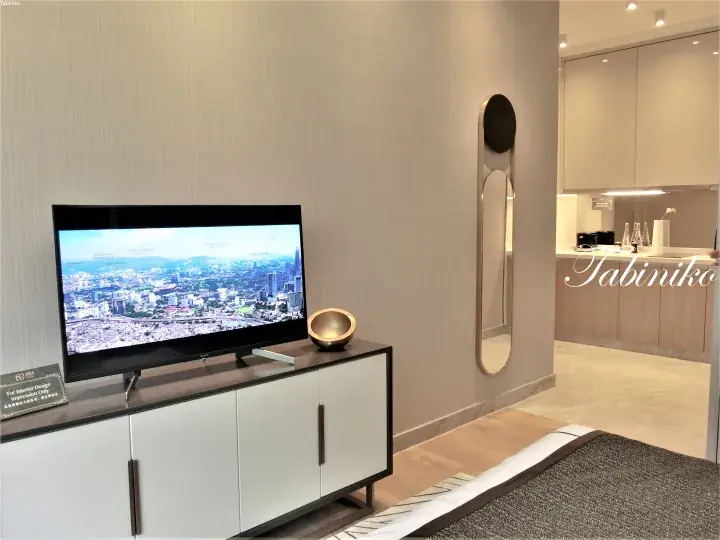 Modern living room with TV displaying Kuala Lumpur skyline, sleek white cabinet, and open kitchen area.