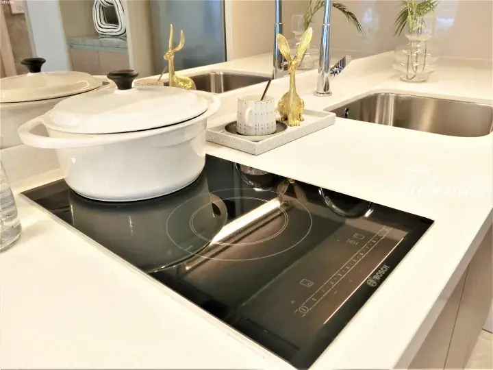 Modern kitchen featuring a white countertop, Bosch induction cooktop, and decorative golden rabbit figurines.
