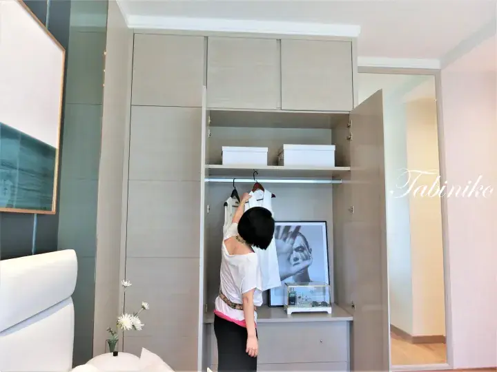 Woman organizing clothes in a modern built-in wardrobe with hanging space and storage boxes.
