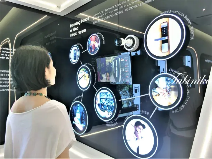 Woman viewing a digital display showcasing smart home security features like CCTV and access control at a property showroom.