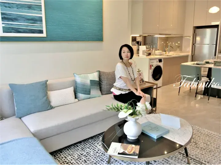 Woman sitting on a modern sofa in a stylish apartment living room with a kitchen and dining area in the background.