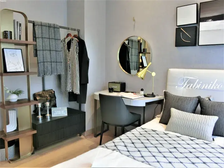 Modern bedroom interior with a white bed, grey desk, and gold accents in a stylish apartment.