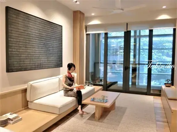 Woman reading a book in a modern minimalist living room with large glass doors and a textured wall art piece.
