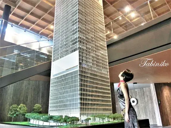 Woman admiring a large architectural model of a modern skyscraper inside a property showroom.