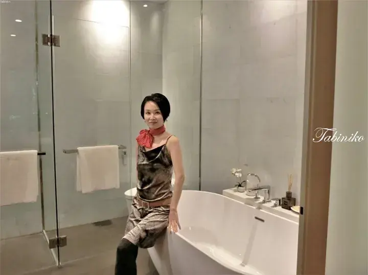 Woman posing in a modern bathroom with a freestanding bathtub and marble walls.
