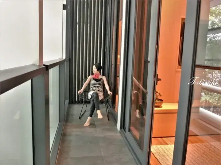 Woman relaxing on a balcony chair with a modern vertical slat wall and glass doors leading to a warm interior.