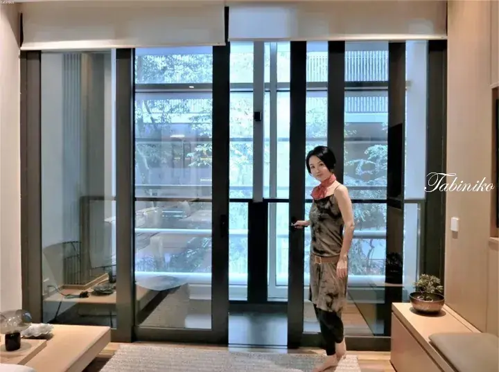 Woman standing by large glass sliding doors in a modern Malaysian home with a view of the garden.