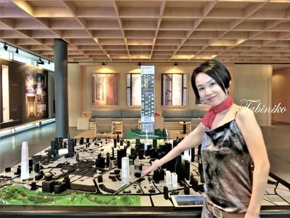A woman points to a detailed property development model at a sales gallery.