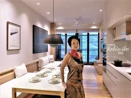 Woman standing in modern open-plan dining and kitchen area with marble table and large windows.