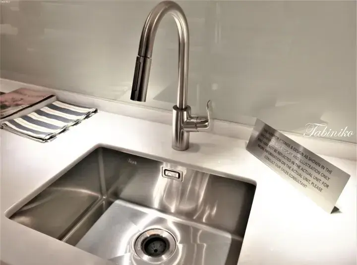 Modern stainless steel kitchen sink with high-arc faucet and white countertop in a property showroom display.