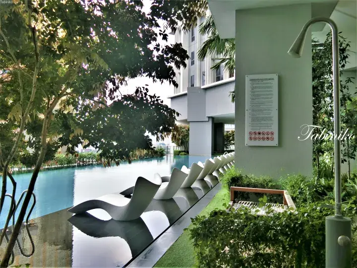 Modern infinity pool with white lounge chairs and lush greenery at a Malaysian residential property.