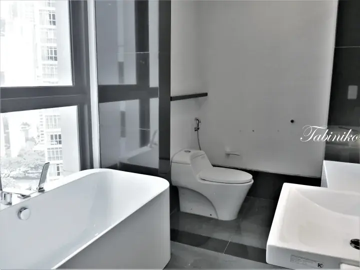 Modern bathroom with a freestanding bathtub, smart toilet, and city view from a high-rise apartment in Malaysia.