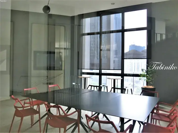 Modern meeting room with large black table, red chairs, and floor-to-ceiling windows overlooking city buildings.