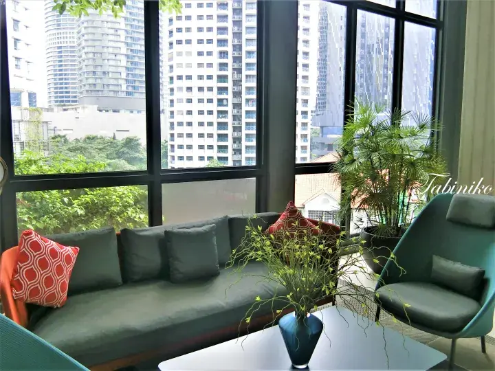 Modern lounge with green sofa and red cushions overlooking lush trees and high-rise buildings in Kuala Lumpur.
