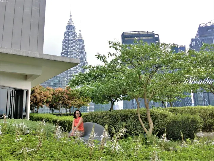 Woman relaxing on a rooftop garden chair with KLCC Petronas Towers view in Kuala Lumpur.