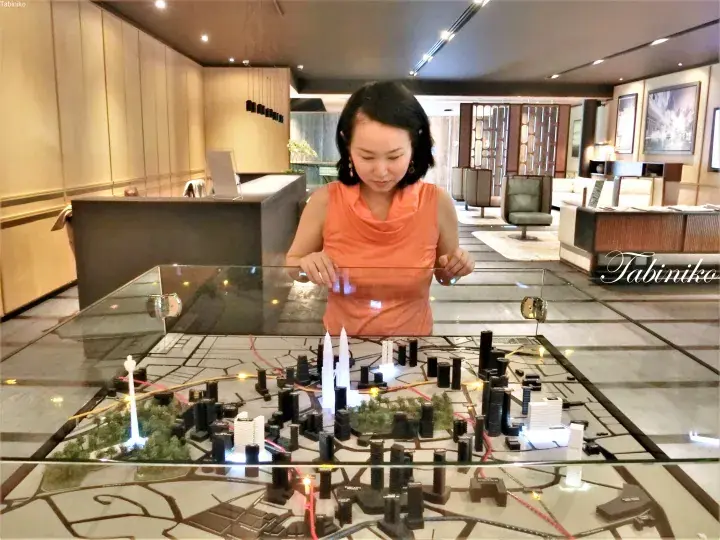 Woman examining a detailed illuminated city model featuring the Petronas Twin Towers in a modern showroom.