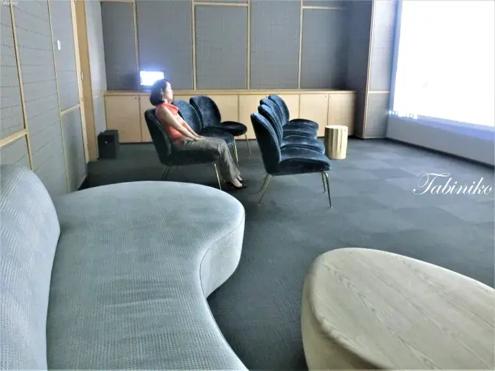 Woman relaxing in a modern lounge with blue velvet chairs and a curved sofa.