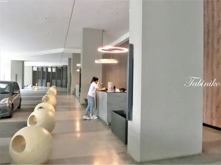 Modern hotel lobby with a guest at the reception desk and a row of spherical decorative seating.