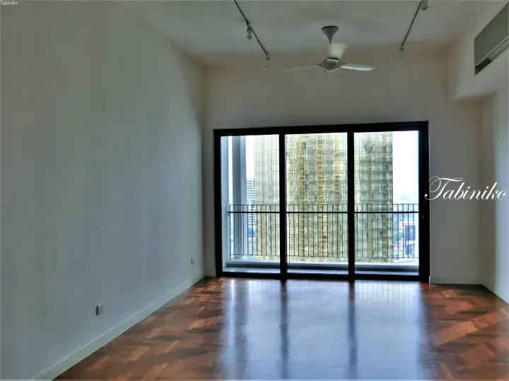Spacious empty room with herringbone wood flooring and large glass doors opening to a balcony with city views.