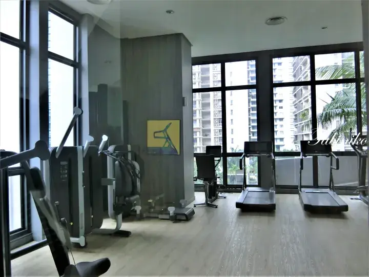 Modern gym with treadmills and weight machines near large windows overlooking high-rise buildings.
