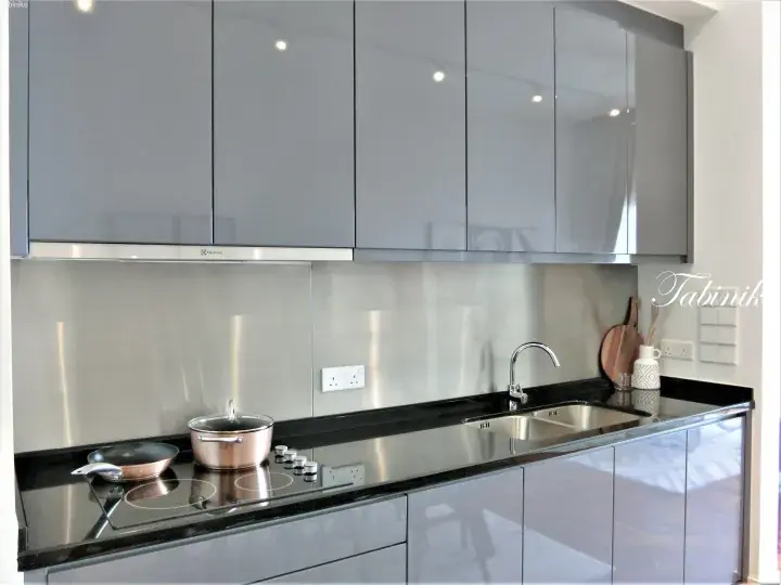 Modern kitchen with glossy grey cabinets, black countertops, stainless steel backsplash, and induction cooktop