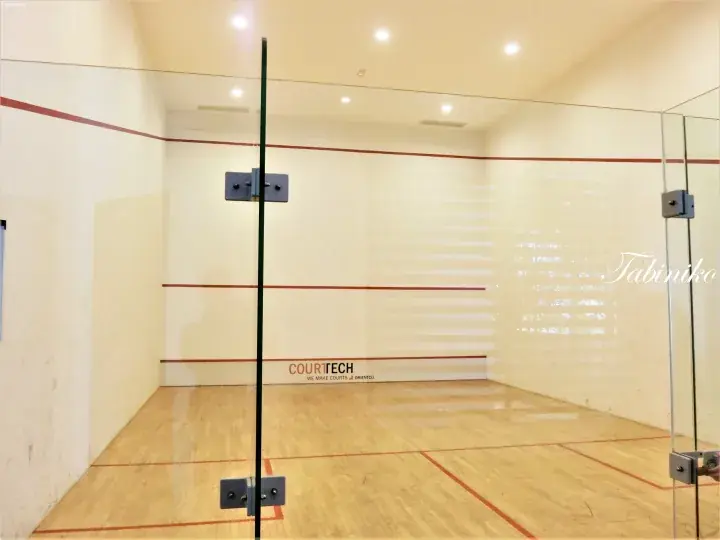 Empty squash court with glass walls, wooden floor, and red boundary lines.