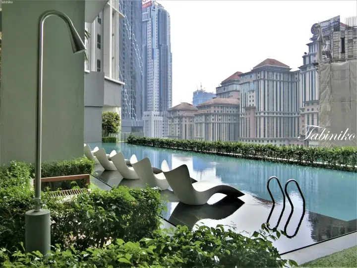 Infinity pool with lounge chairs at a KLCC property, overlooking the Menara Maxis skyscraper and KLCC Park.