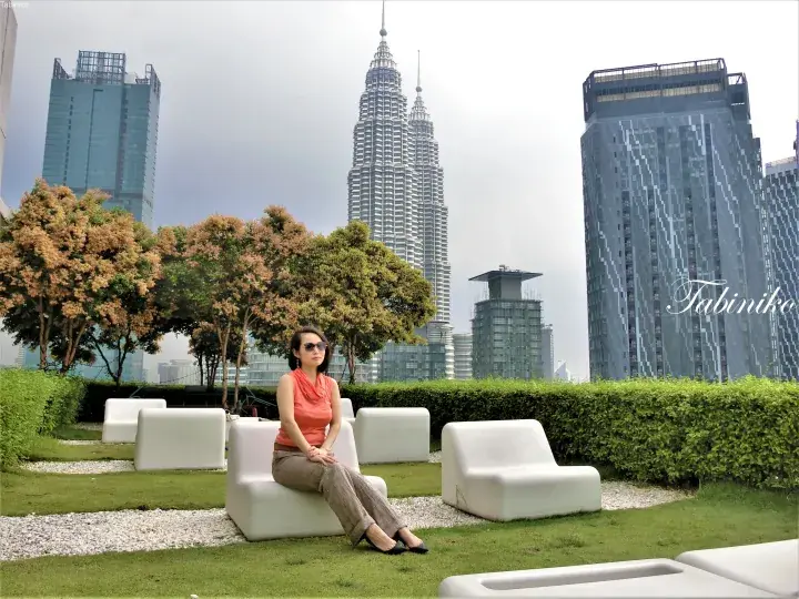 Woman relaxing on a rooftop lounge chair with a view of the Petronas Twin Towers and KLCC skyline.