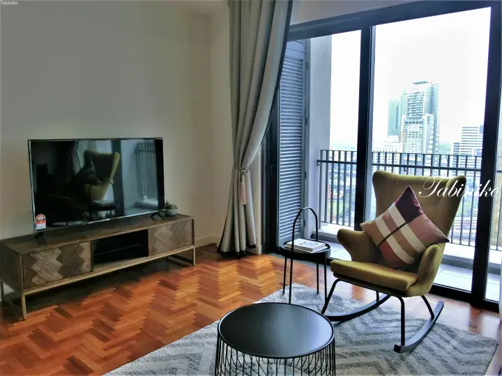 Modern apartment living room with herringbone flooring, TV console, and yellow rocking chair overlooking city skyline