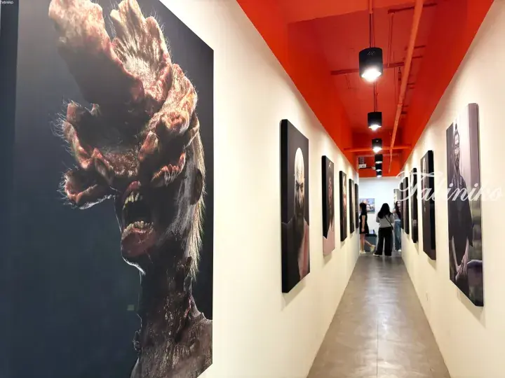 Gallery hallway with red ceiling displaying large zombie artwork and portraits, with visitors viewing the exhibition.