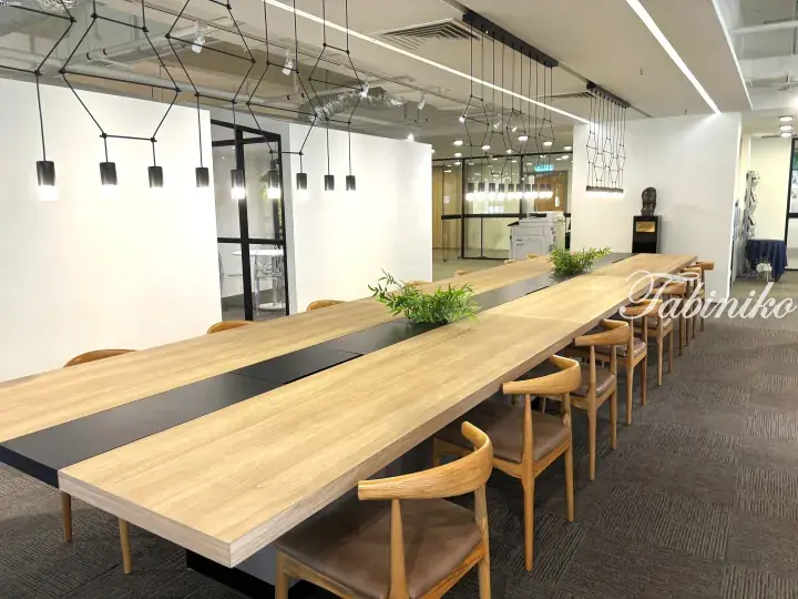 Modern office meeting room with a long wooden table, wooden chairs, and geometric pendant lights.