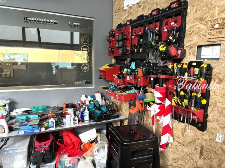 Organized workshop wall with Milwaukee Packout tool storage, safety signage, and workbench supplies.